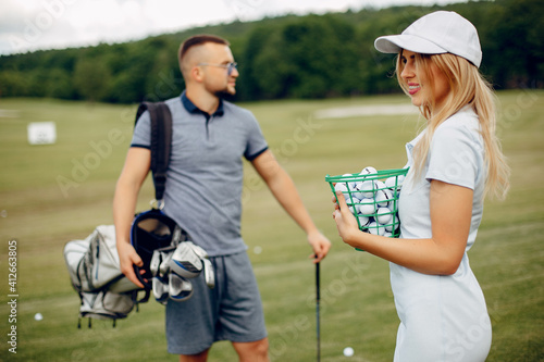 Couple in a golf course. Blonde in a sport clothes. Pair playing golf