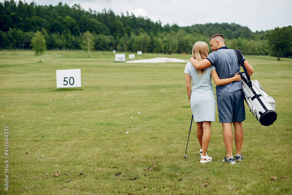 Couple in a golf course. Blonde in a sport clothes. Pair playing golf Couple in a golf course. Blonde in a sport clothes. Pair playing golf