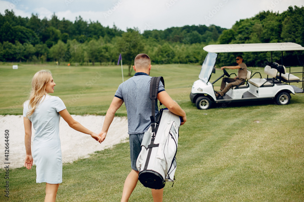 Fototapeta premium Couple in a golf course. Blonde in a sport clothes. Pair playing golf