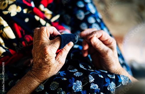 Hands of an elderly woman sewing a red garment seen from close up, very detailed. Concept of old age and something handmade.