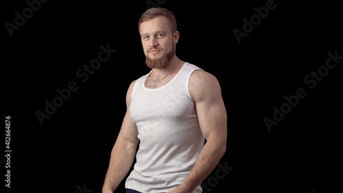 Caucasian sporty man stands sideways in a tank top on a black background. One man is a model. High quality photo © Vladimir