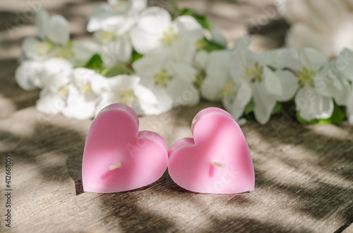 Valentines day card, two pink candles in the form of hearts on a wooden background with apple tree flowers