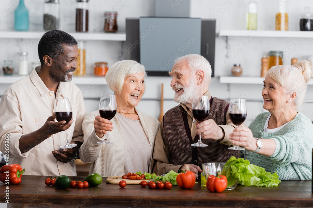 joyful multicultural pensioners holding glasses on wine near vegetables on table joyful multicultural pensioners holding glasses on wine near vegetables on table