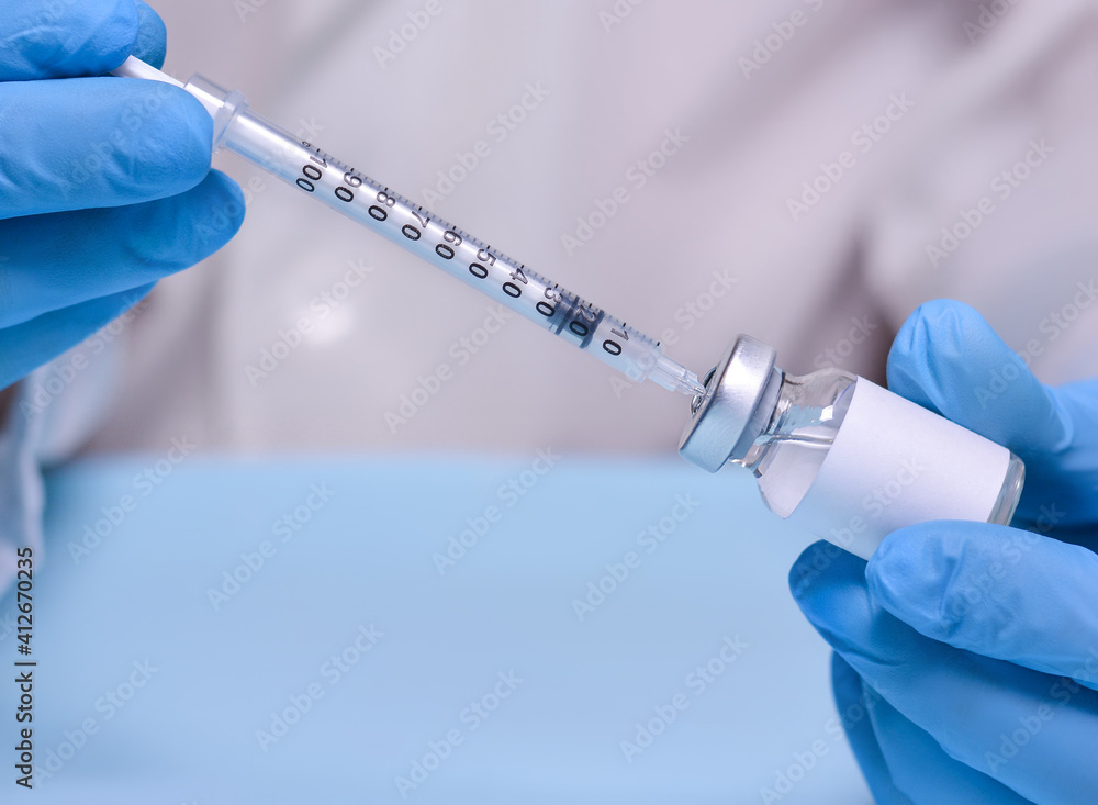 Doctor in protective medical gloves holds a vial with a vaccine and a syringe.The concept of medicine, healthcare and science.Coronavirus vaccine.Copy space for text. Doctor in protective medical gloves holds a vial with a vaccine and a syringe.The concept of medicine, healthcare and science.Coronavirus vaccine.Copy space for text.