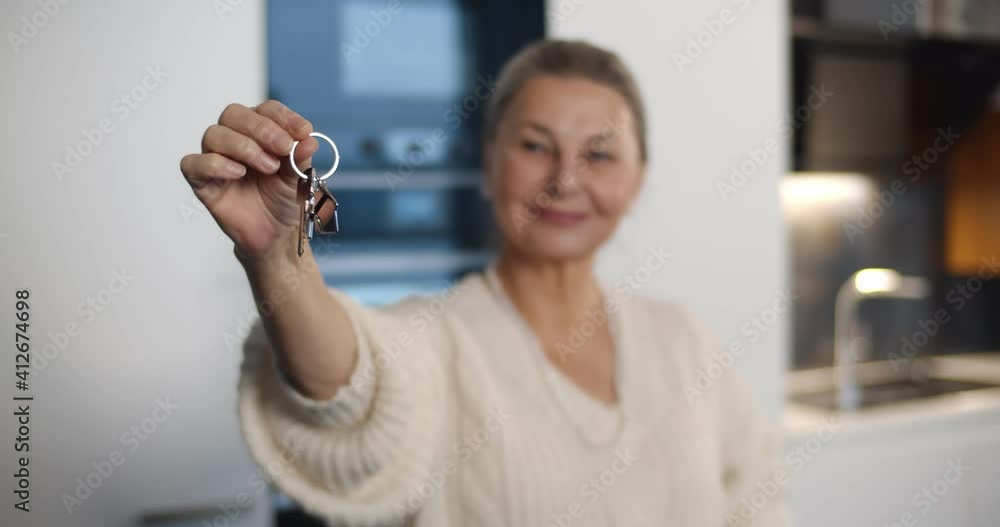 Portrait of smiling senior woman showing keys to new house at camera Portrait of smiling senior woman showing keys to new house at camera