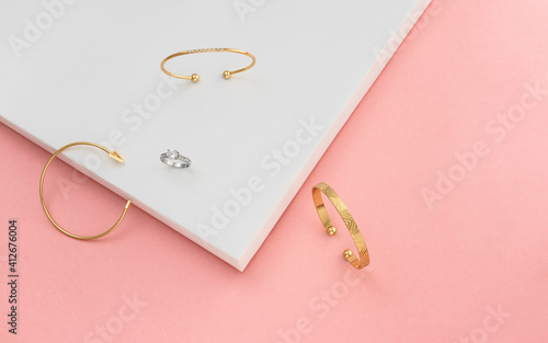 Top view of three bracelets and ring on pink and white background
