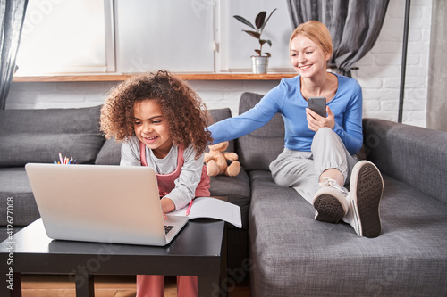 Mother and daughter studying online together in living room