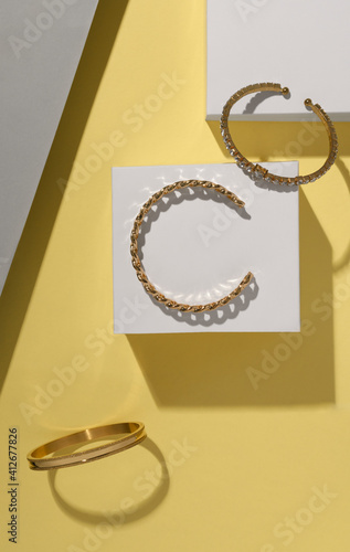 Flat lay of golden bracelets on white cubes on yellow background