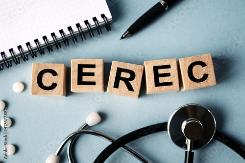 Wooden cubes with the inscription CEREC lie on the table. View from above. Nearby is a stethoscope, a notebook and scattered pills.