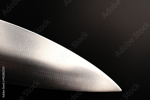 The blade of a large knife on a black background. Dimmed lights.