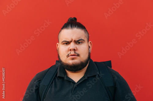 Close photo of a gloomy man with a beard and overweight on a red background, looking anxiously at the camera.