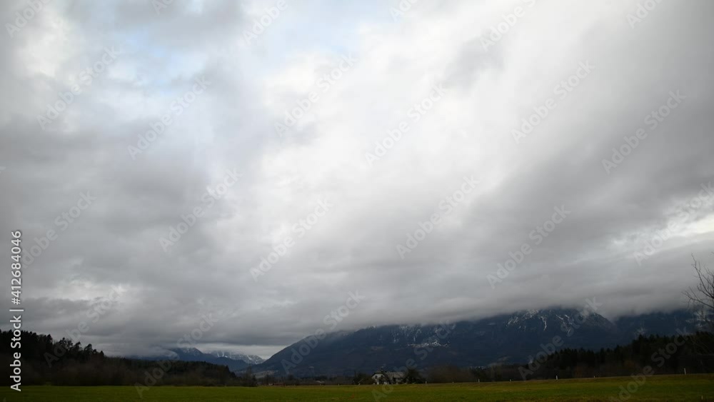 Time lapse view of clouds moving over Alps mountains in Slovenia. Farming field in foreground. Gloomy grey weather. Static shot Time lapse view of clouds moving over Alps mountains in Slovenia. Farming field in foreground. Gloomy grey weather. Static shot
