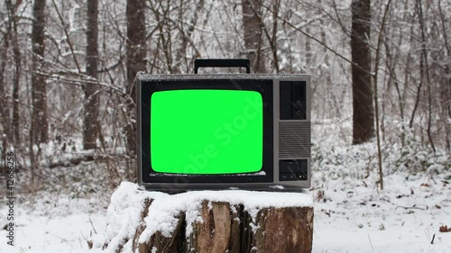 Old vintage tv with green screen on old stump white is snowing in winter season 
