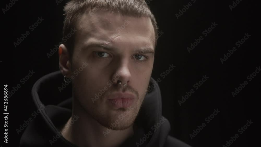 Brutal man in dark hoodie, posing at boxing club with gloves for training. Serious professional sport portrait. Brutal man in dark hoodie, posing at boxing club with gloves for training. Serious professional sport portrait.