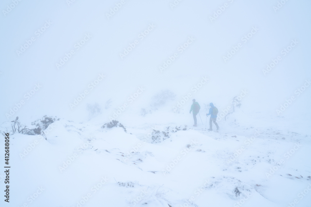 IMAGE OF TWO PEOPLE HIKING IN EXTREME CONDITIONS. ALPINISTS TREKKING IN HARSH WINTER CONDITIONS. COLD AND BAD WEATHER CONCEPT