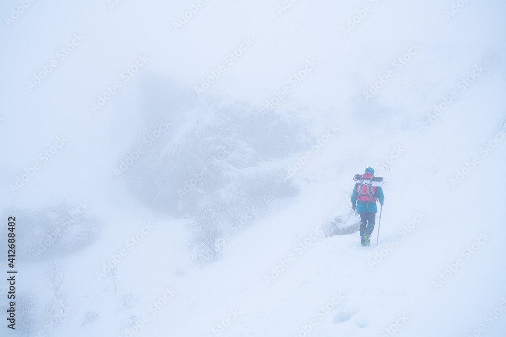 IMAGE OF A PERSON HIKING IN EXTREME CONDITIONS. ALPINIST TREKKING IN HARSH WINTER CONDITIONS. COLD AND BAD WEATHER CONCEPT