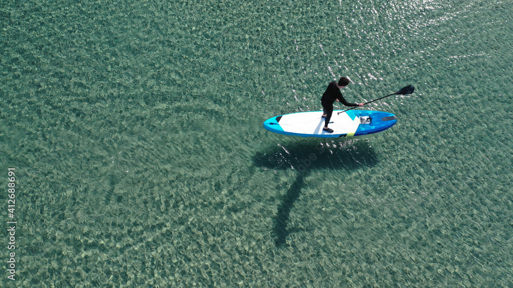 Aerial drone photo of fit man on SUP or Stand Up Paddle board in tropical exotic emerald calm sea bay