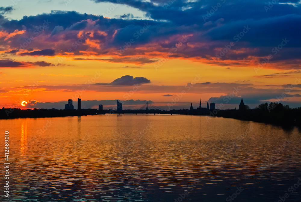 sunset. in the photo, the clouds are illuminated by the evening sun,in the foreground is a river, in the background is a city