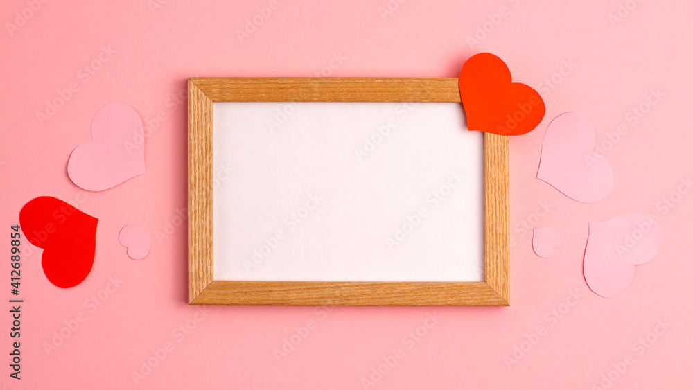 Red and pink paper hearts on and near wooden frame on pink background at the centre side Valentine's day love relationship romantic anniversary wedding holiday concepts Flat lay copy space mockup