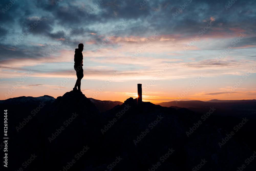 PERSON STANDING AT THE TOP OF A MOUNTAIN. MAN ENJOYING AND HAVING FUN DURING SUNSET. OUTDOOR AND SUNSET CONCEPT.