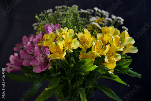 Blooming bouquet of colourful vibrant flowers in a clear vase against a black background. 