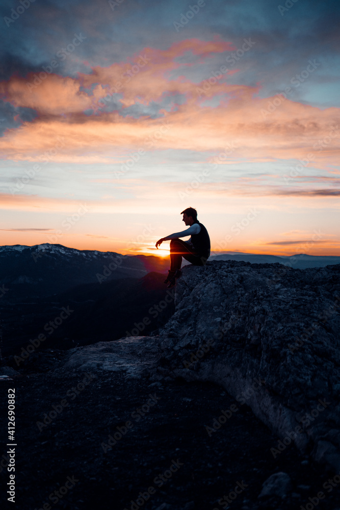 Obraz premium PERSON SITTING AT THE TOP OF A MOUNTAIN. MAN ENJOYING AND HAVING FUN DURING SUNSET. OUTDOOR AND SUNSET CONCEPT.