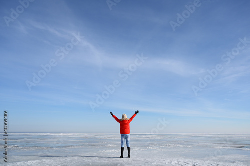 Woman in red jacket standing on frozen lake with holding up hands © Anatoliy Sadovskiy