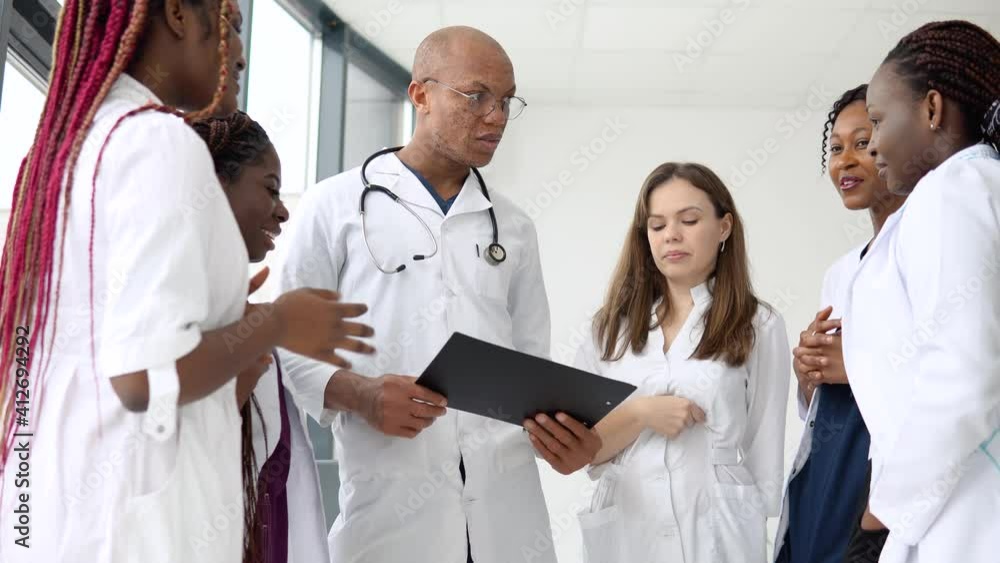 A team of doctors, including international man and women, have a business conversation while standing in a clinic A team of doctors, including international man and women, have a business conversation while standing in a clinic