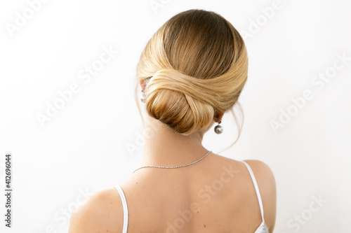 Hair stylist makes a beautiful hairstyle for a girl on a light background