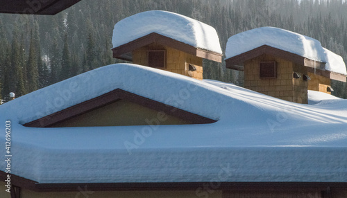 snow covered roof tops of ski chalets in ski village on cold sunny day outside with heavy snow fall triangular shapes of home exterior and vents on house 
