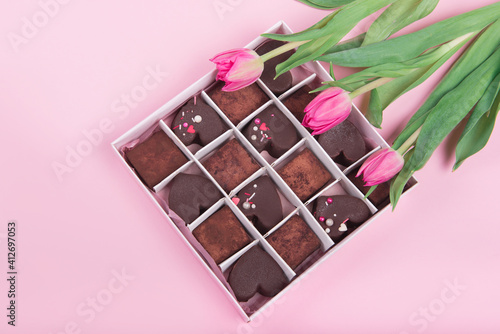 Present box with chocolate sweets hearts and tulips on pink background. Desert for Valentine Day