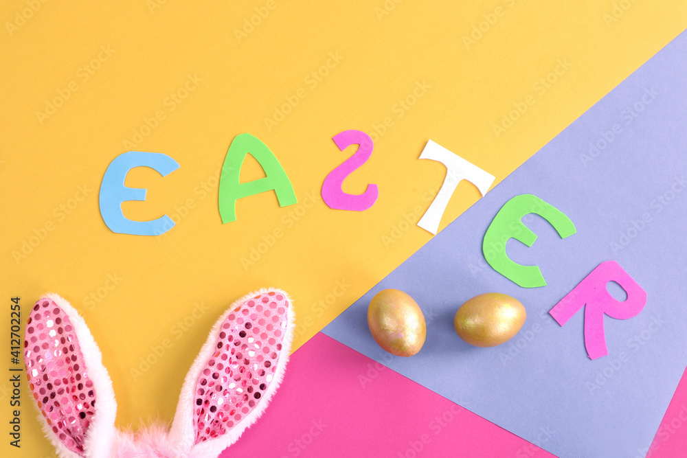 Paper letters folded with the word Easter, rabbit ears and golden eggs on a multicolored background - the concept of celebrating Easter