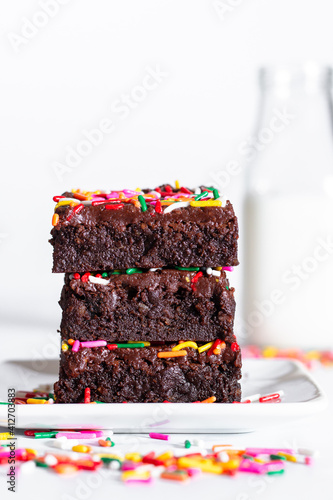 homemade chocolate frosted brownies with rainbow colored sprinkles on a white background