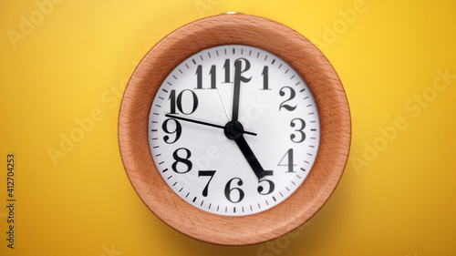 Wooden round clock on yellow background.