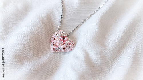 A beautiful pale pink heart pendant with a silver chain, isolated and contrasted against a white bed spread in London, Ontario, Canada.