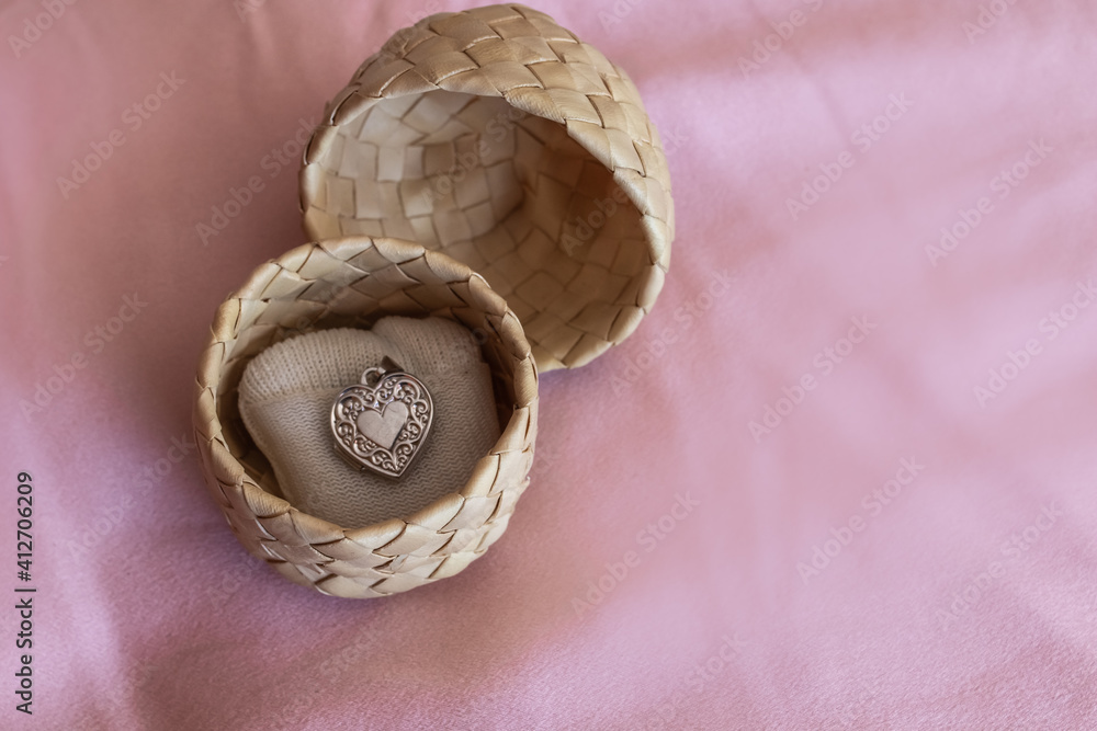 A silver heart-shaped locket on a small white pillow in a woven palm ring box on a pink silk pillowcase, London, Ontario, Canada.