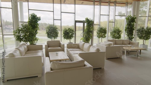 No people arc shot of posh lounge zone with beige leather sofas and panoramic windows with picturesque view on green lawn
