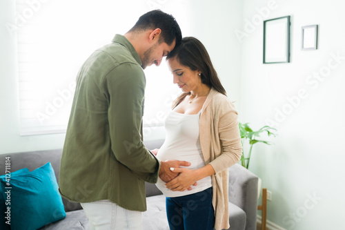 Adorable pregnant wife and husband holding hands an touching the belly
