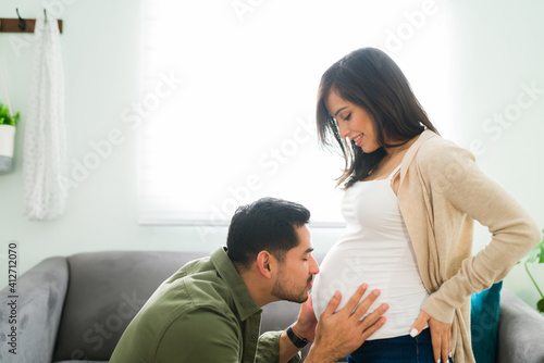 Adorable parent giving a kiss to the belly of a pregnant woman