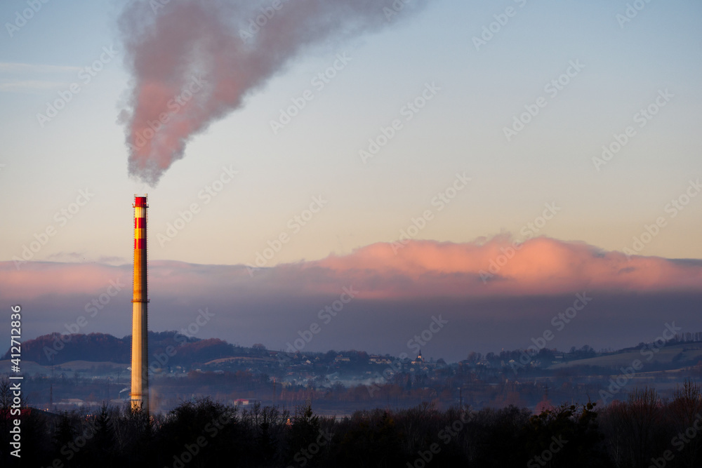 Steaming factory chimney with landscape in the background.