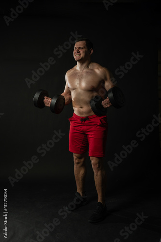 Fitness man presses dumbbells in red panties confident caucasian smart, happy. Happiness model, dumbbells cool background black bodybuilder