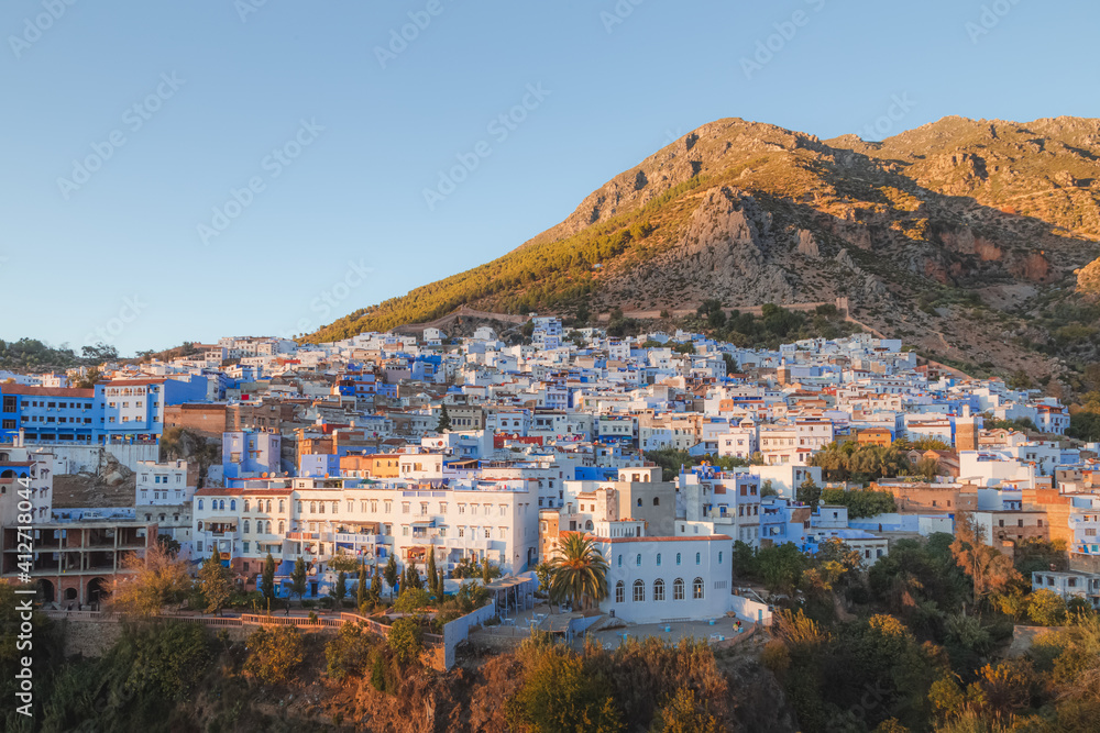 A scenic sunset or sunrise cityscape view over Chefchaouen, Morocco, known as the Blue Pearl with its shades of blue on the town's historic buildings.
