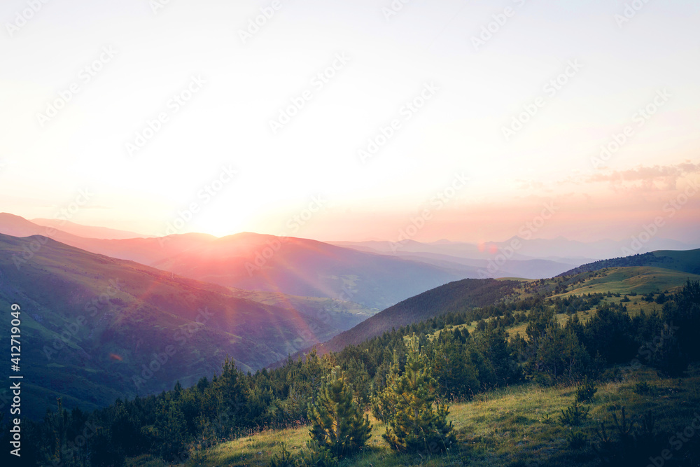 Beautiful sunrise on top of the mountain with fir trees. A new day begins. Sunbeams in the golden hour. Concept of nature, holidays, and healthy lifestyle. Landscape view with blank space for text.