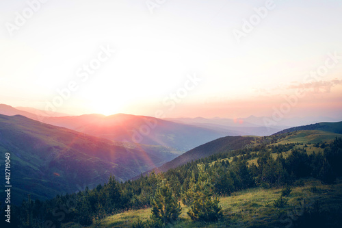 Beautiful sunrise on top of the mountain with fir trees. A new day begins. Sunbeams in the golden hour. Concept of nature, holidays, and healthy lifestyle. Landscape view with blank space for text.
