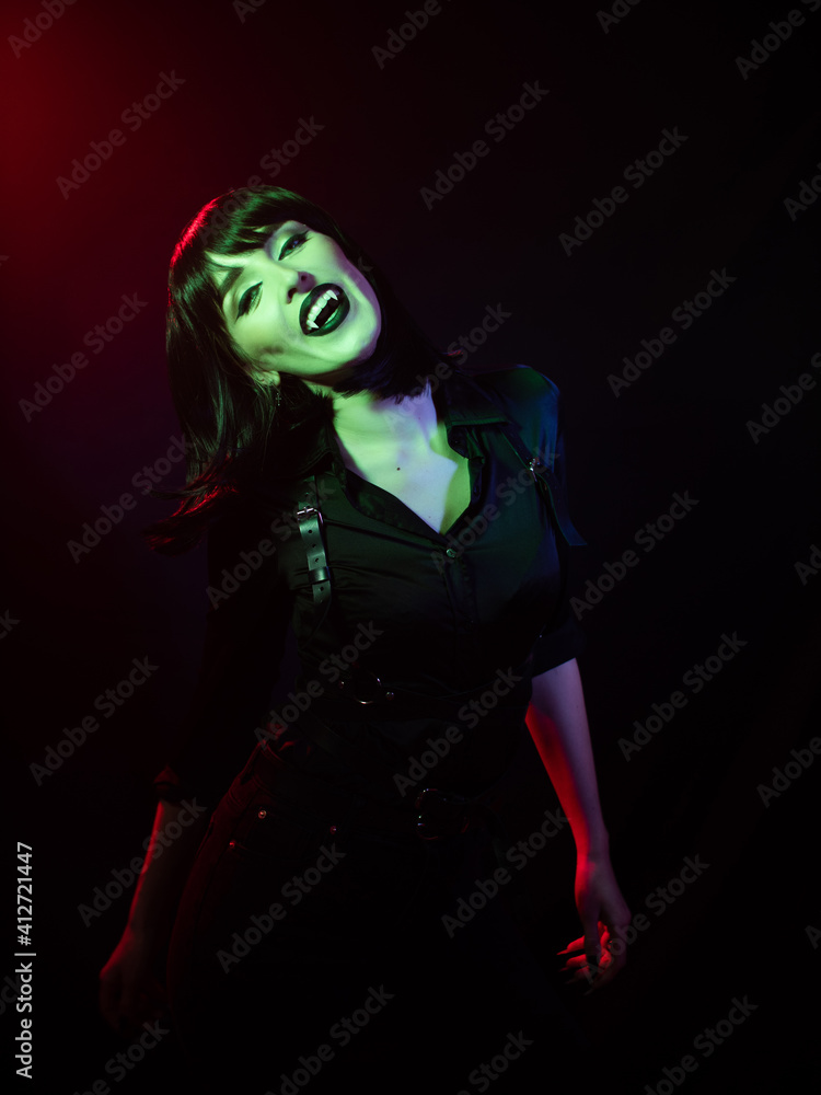 girl in green-red with vampire fangs on a dark background