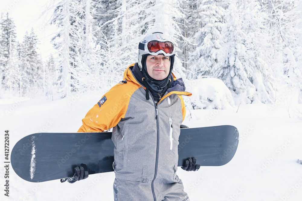 Man with a snowboard standing on a mountain on the background of the winter forest. Winter leisure activity. Healthy lifestyle. Extreme sports.