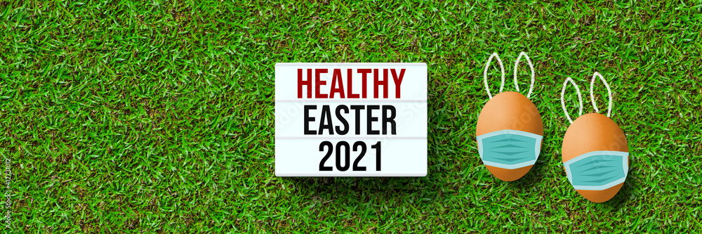 lightbox with message HEALTHY EASTER 2021 with easter eggs covered by a face mask on grass background