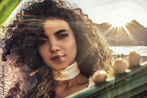 Beauty portrait of sensual hispanic woman on the beach during sunset. Girl with afro hairstyle looking at camera. Delicate glamour makeup. photo