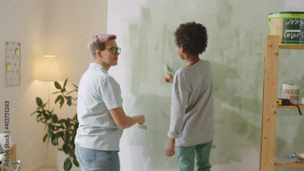 Back view of Caucasian mother and mixed raced little son painting wall together in green color and speaking while renovating home Back view of Caucasian mother and mixed raced little son painting wall together in green color and speaking while renovating home