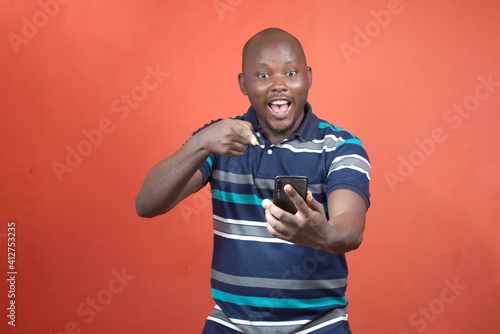 A happy African guy amazed as he points into the smartphone in his hand 